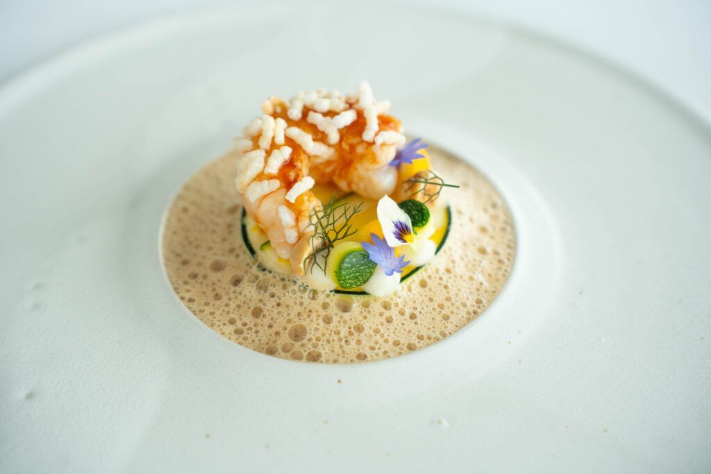 Foodfotografie langoustine met schuim Langoustine met gepofte rijst, courgette en eetbare bloemen in een schuimige saus
