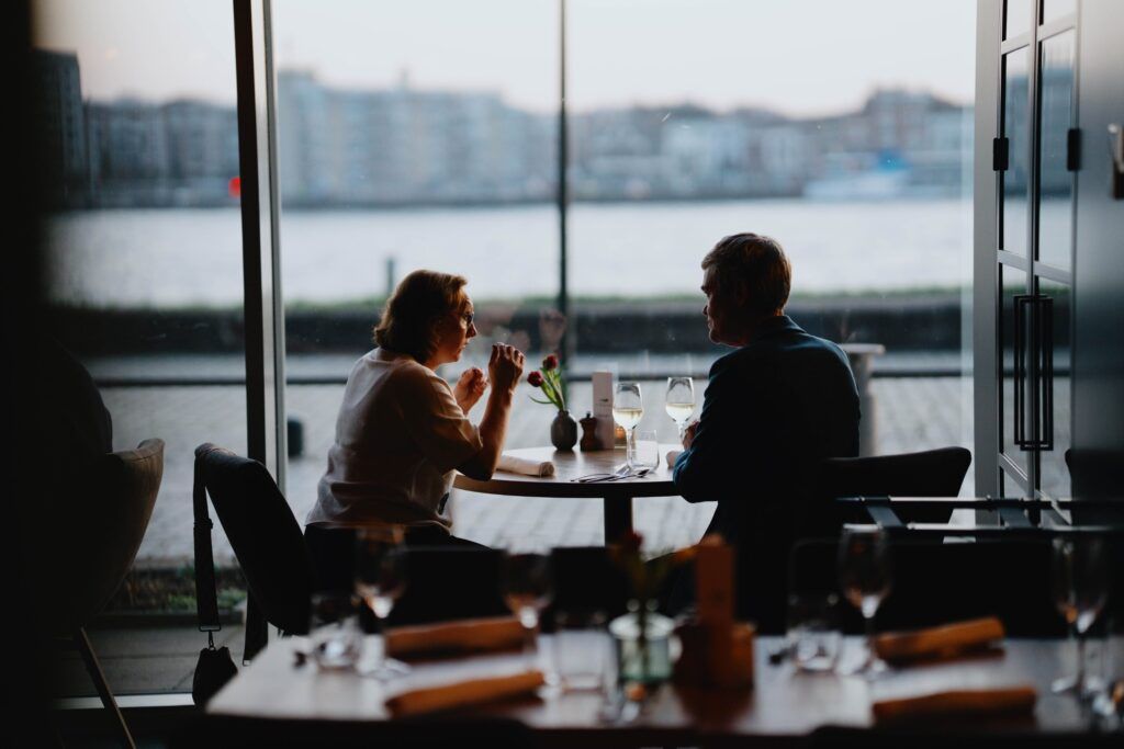 Koppel dineert aan het raam met zicht op het water Koppel aan een tafel bij het raam van een restaurant met zicht op de rivier bij valavond
